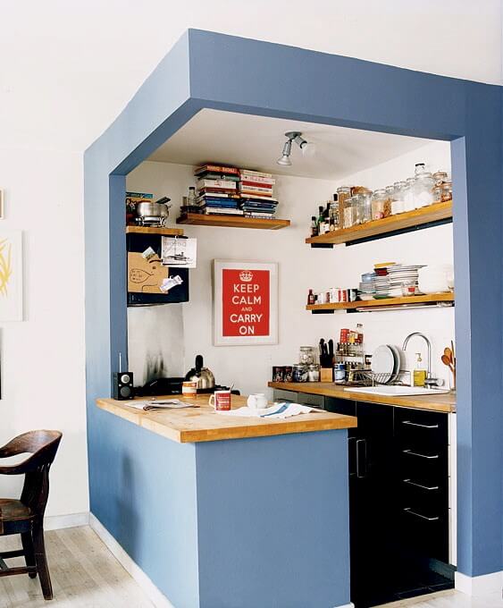 A small kitchen with storage on walls and book shelf on top