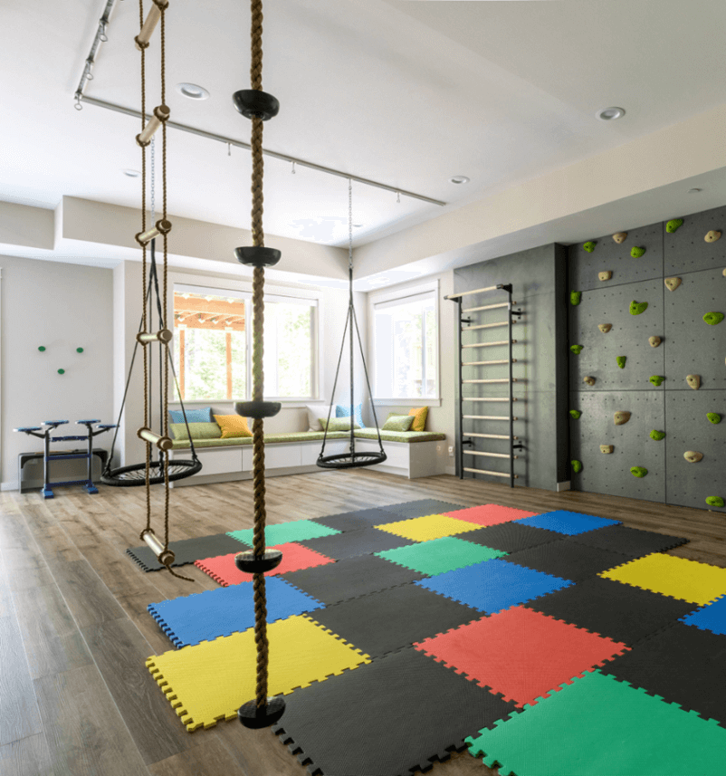 A room filled with rock climbing walls, swings and rubber mat for kids to play
